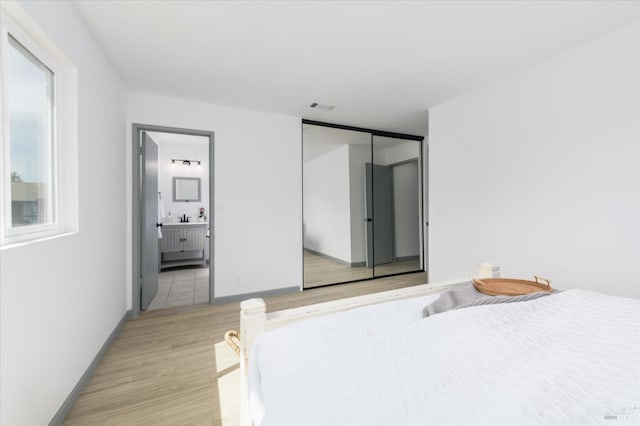 bedroom with baseboards, visible vents, ensuite bathroom, and light wood finished floors