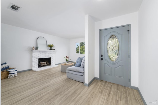 entryway featuring baseboards, a brick fireplace, light wood-type flooring, and visible vents