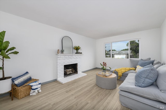 living room featuring baseboards, a brick fireplace, and wood finished floors