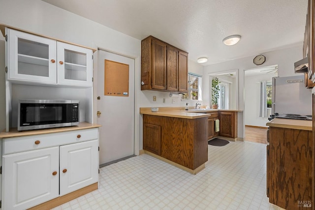 kitchen featuring light countertops, stainless steel microwave, a peninsula, and white cabinetry