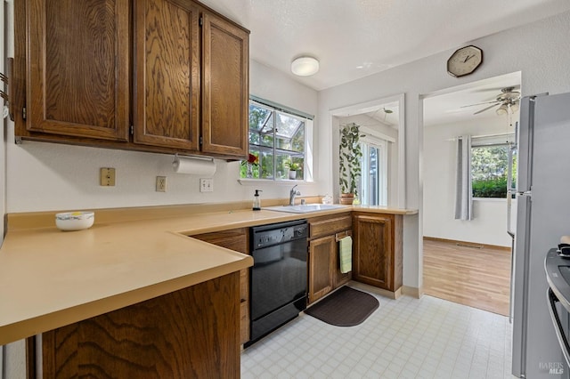 kitchen with freestanding refrigerator, a peninsula, black dishwasher, light countertops, and a sink
