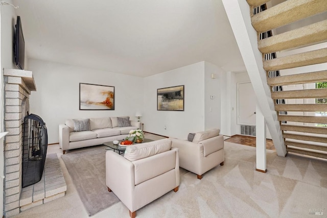 carpeted living area featuring a brick fireplace, stairs, and visible vents