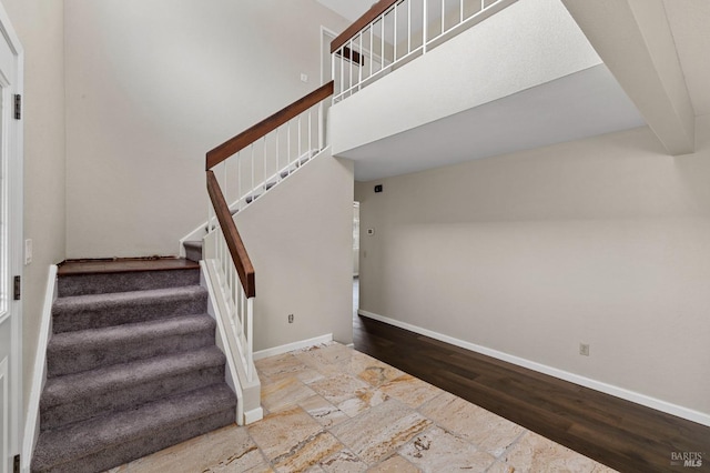 staircase featuring baseboards, a towering ceiling, and wood finished floors