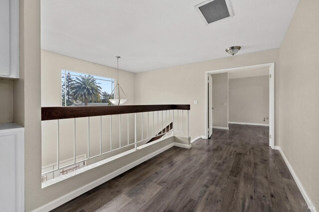 corridor with visible vents, baseboards, wood finished floors, and an upstairs landing