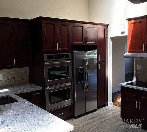 15 Main Dr, San Rafael, CA 94901 - kitchen with under cabinet range hood, light stone counters, fridge with ice dispenser, double oven, and tasteful backsplash