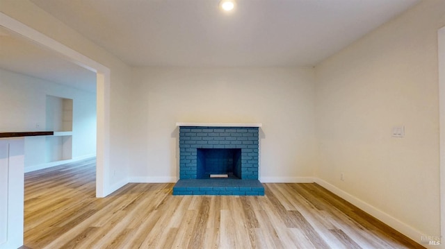 unfurnished living room featuring baseboards, a brick fireplace, and wood finished floors