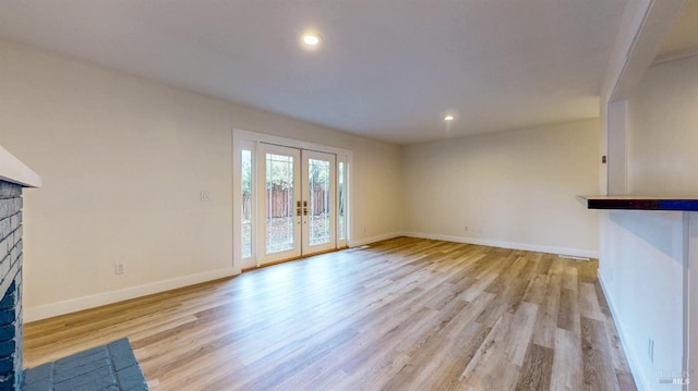 unfurnished living room with light wood-style floors, baseboards, a brick fireplace, and french doors