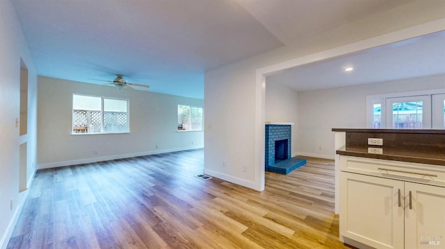 unfurnished living room featuring a ceiling fan, visible vents, a fireplace, baseboards, and light wood finished floors