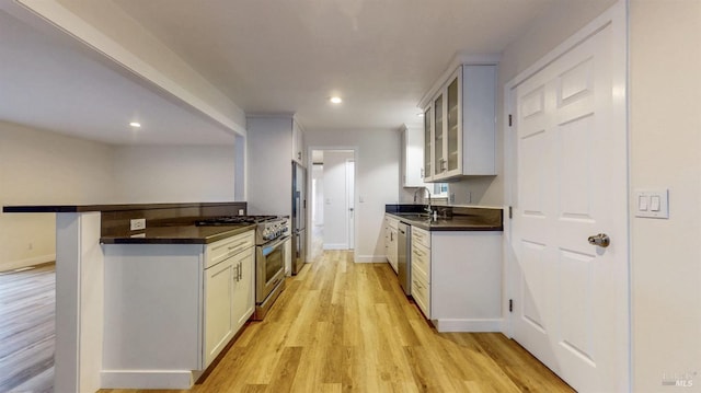 kitchen featuring dark countertops, appliances with stainless steel finishes, a sink, light wood-style floors, and glass insert cabinets