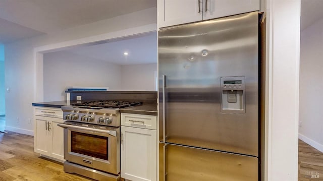 kitchen featuring light wood-type flooring, white cabinetry, appliances with stainless steel finishes, and dark countertops
