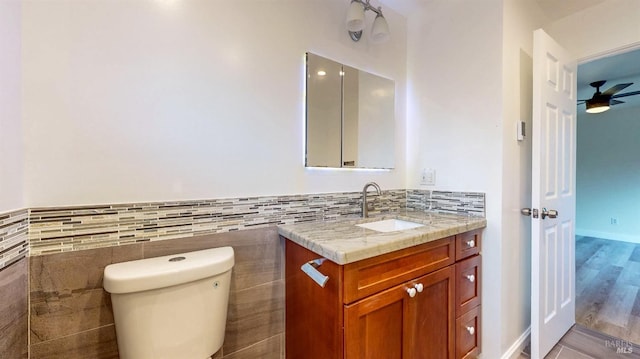 bathroom featuring ceiling fan, tile walls, wainscoting, vanity, and toilet