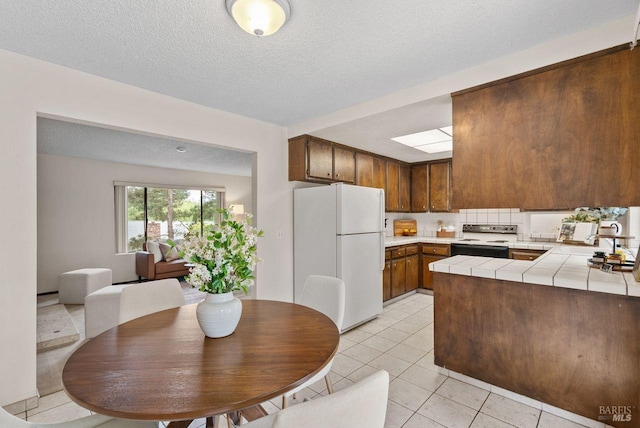 kitchen with a sink, tile counters, a textured ceiling, range with electric cooktop, and freestanding refrigerator