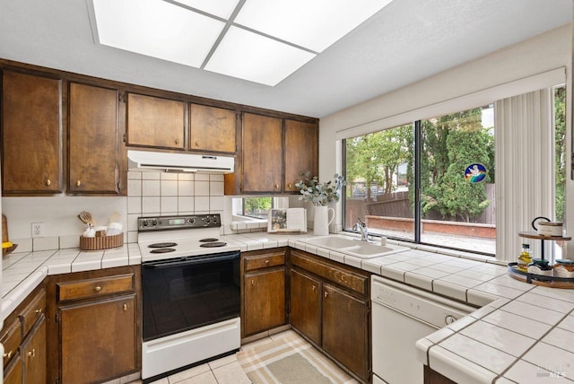 kitchen with decorative backsplash, white appliances, under cabinet range hood, a sink, and light tile patterned floors
