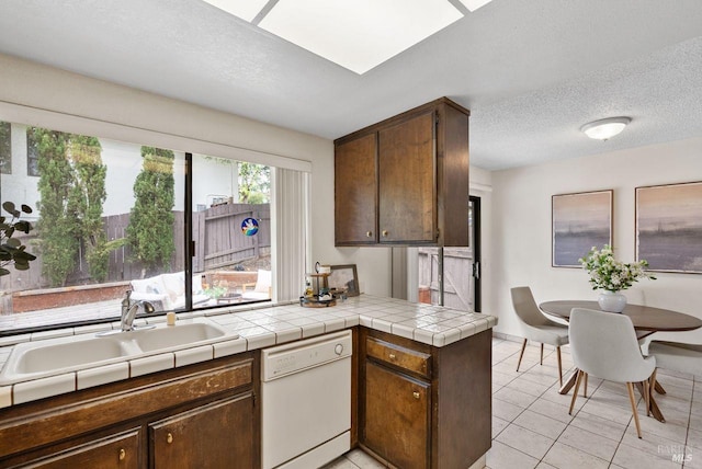 kitchen featuring a sink, dishwasher, a textured ceiling, a peninsula, and light tile patterned floors