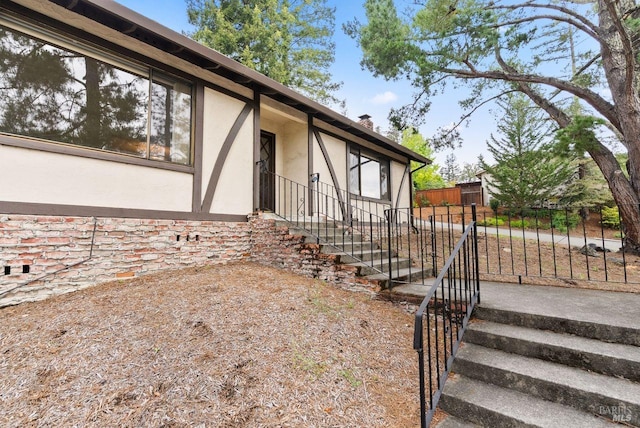 view of exterior entry featuring stucco siding, a chimney, and fence