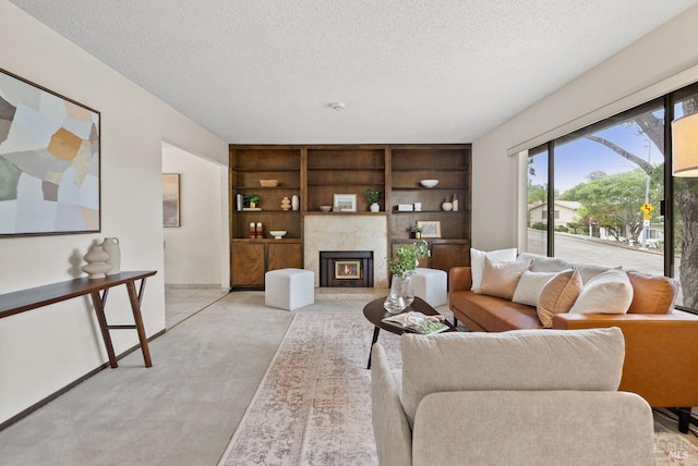 living room with a textured ceiling, light colored carpet, built in shelves, and a fireplace