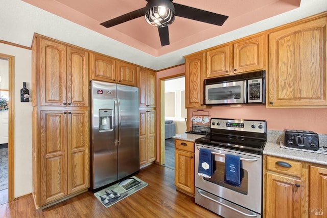kitchen with ceiling fan, appliances with stainless steel finishes, wood finished floors, and a raised ceiling