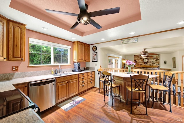 kitchen with a ceiling fan, stainless steel dishwasher, brown cabinets, a sink, and a raised ceiling