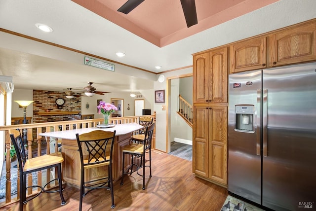 kitchen with crown molding, a brick fireplace, light wood-style flooring, a ceiling fan, and stainless steel refrigerator with ice dispenser