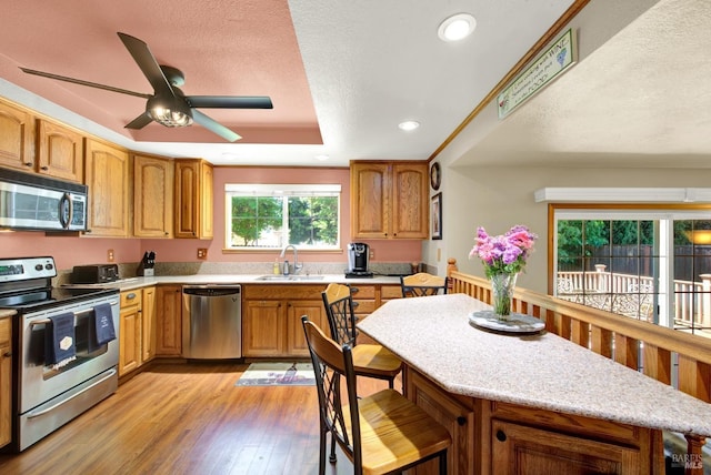 kitchen featuring a sink, a textured ceiling, light wood-style flooring, stainless steel appliances, and a ceiling fan