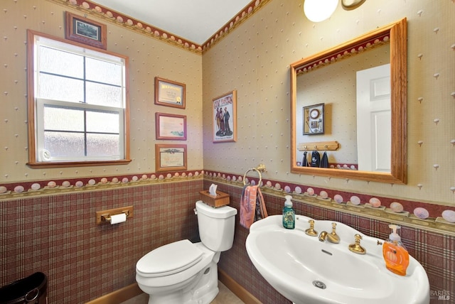 bathroom featuring a sink, toilet, a wainscoted wall, wallpapered walls, and tile walls
