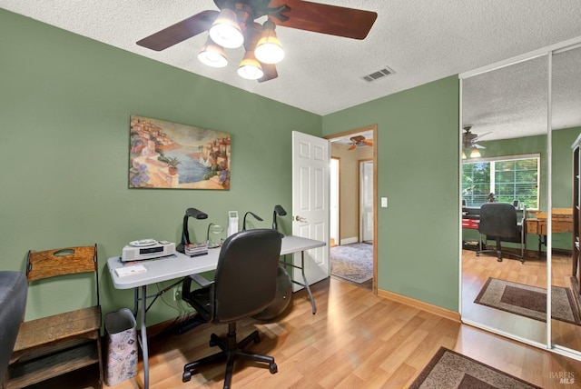 office with a ceiling fan, a textured ceiling, visible vents, and wood finished floors