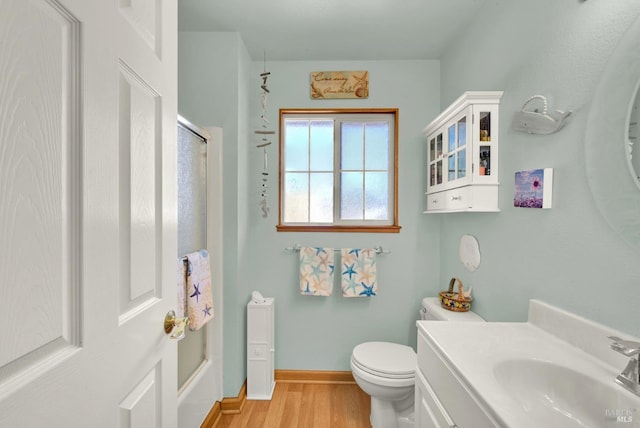 bathroom with walk in shower, wood finished floors, vanity, baseboards, and toilet