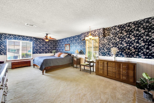 bedroom with visible vents, wainscoting, wallpapered walls, light colored carpet, and a textured ceiling
