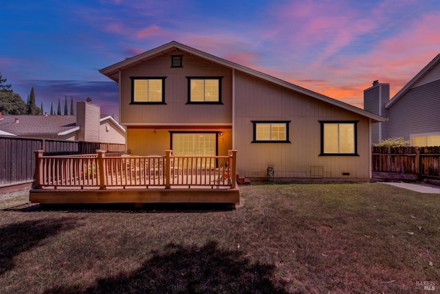 back of property at dusk with fence, a yard, and a deck