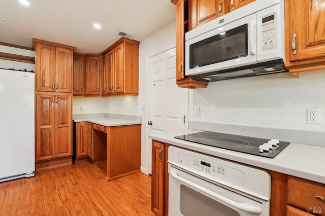 kitchen with brown cabinetry, visible vents, light countertops, light wood-style floors, and white appliances