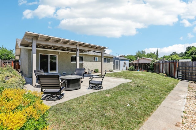 rear view of house featuring a shed, a yard, a patio, a fire pit, and stucco siding