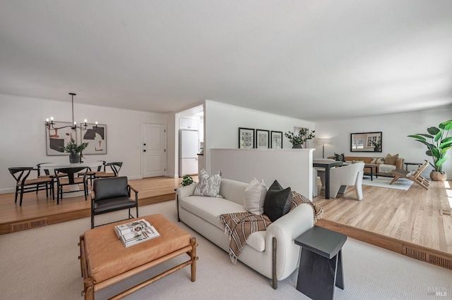 living area with an inviting chandelier, light wood-style flooring, and visible vents