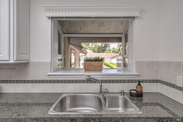 room details featuring a sink, decorative backsplash, dark countertops, and white cabinetry