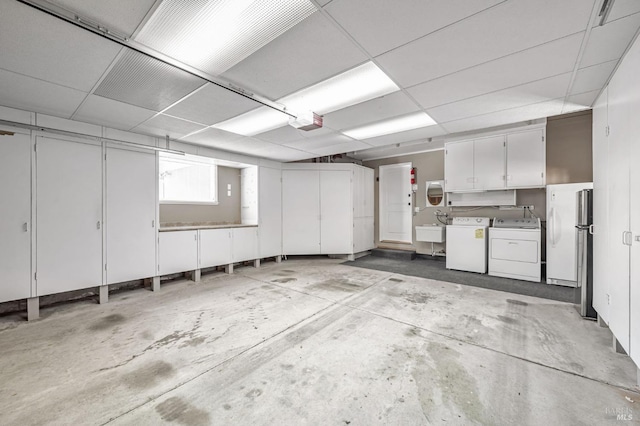 garage featuring a sink, a garage door opener, freestanding refrigerator, and washer and dryer