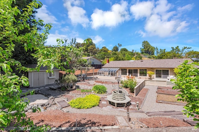 rear view of property featuring a patio, an outdoor structure, a garden, and a shed
