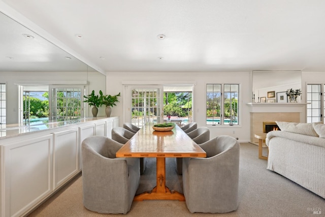 dining area featuring baseboards, light carpet, and a lit fireplace