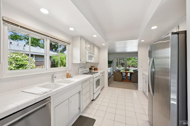 kitchen with recessed lighting, tile countertops, a sink, light tile patterned floors, and stainless steel appliances