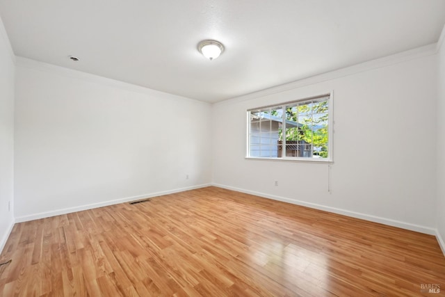 unfurnished room with baseboards, ornamental molding, light wood-style floors, and visible vents