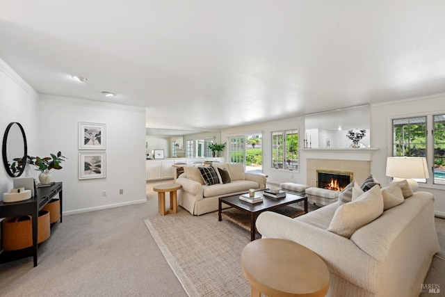 living area with a tiled fireplace, crown molding, a healthy amount of sunlight, and light colored carpet