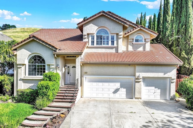 mediterranean / spanish home with a tiled roof, an attached garage, driveway, and stucco siding