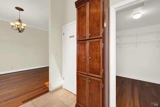 hallway with an inviting chandelier, baseboards, ornamental molding, and light wood finished floors
