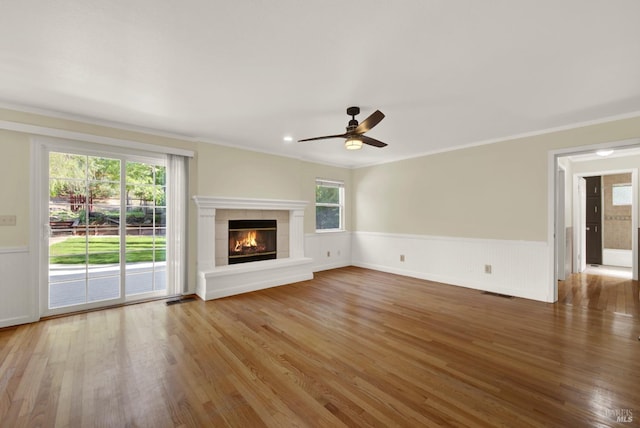 unfurnished living room with crown molding, wainscoting, a ceiling fan, wood finished floors, and visible vents