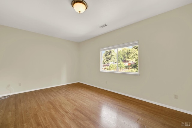 empty room featuring baseboards, visible vents, and wood finished floors