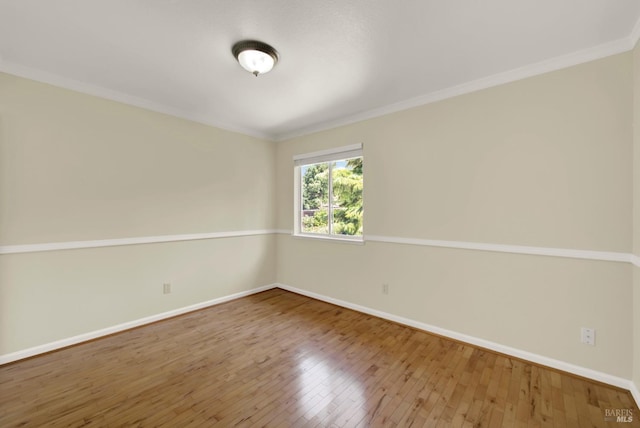 empty room featuring wood-type flooring, baseboards, and crown molding
