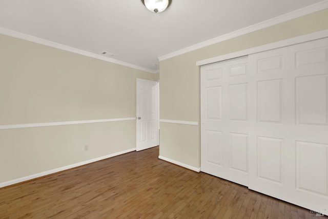 unfurnished bedroom featuring visible vents, crown molding, wood finished floors, baseboards, and a closet