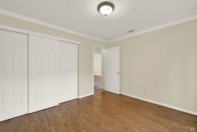 unfurnished bedroom featuring baseboards, wood finished floors, visible vents, ornamental molding, and a closet