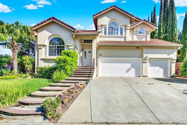 mediterranean / spanish house featuring a tiled roof, an attached garage, driveway, and stucco siding