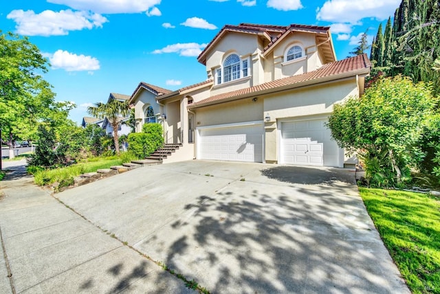 mediterranean / spanish home featuring a garage, stucco siding, a tile roof, and concrete driveway