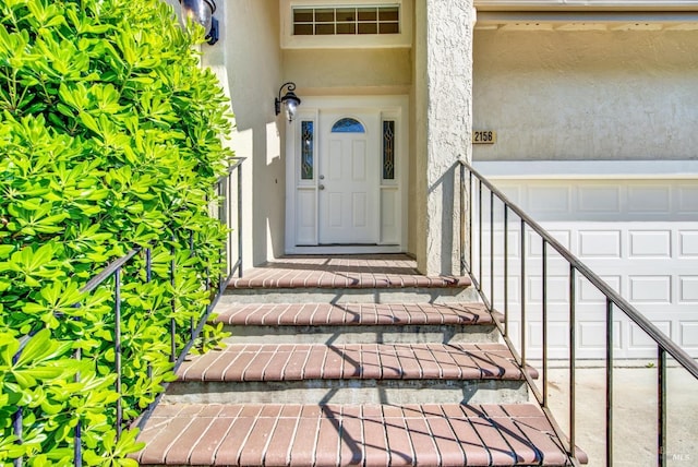 view of exterior entry with a garage and stucco siding