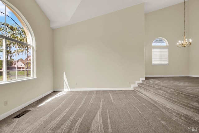 carpeted empty room featuring high vaulted ceiling, baseboards, a notable chandelier, and visible vents